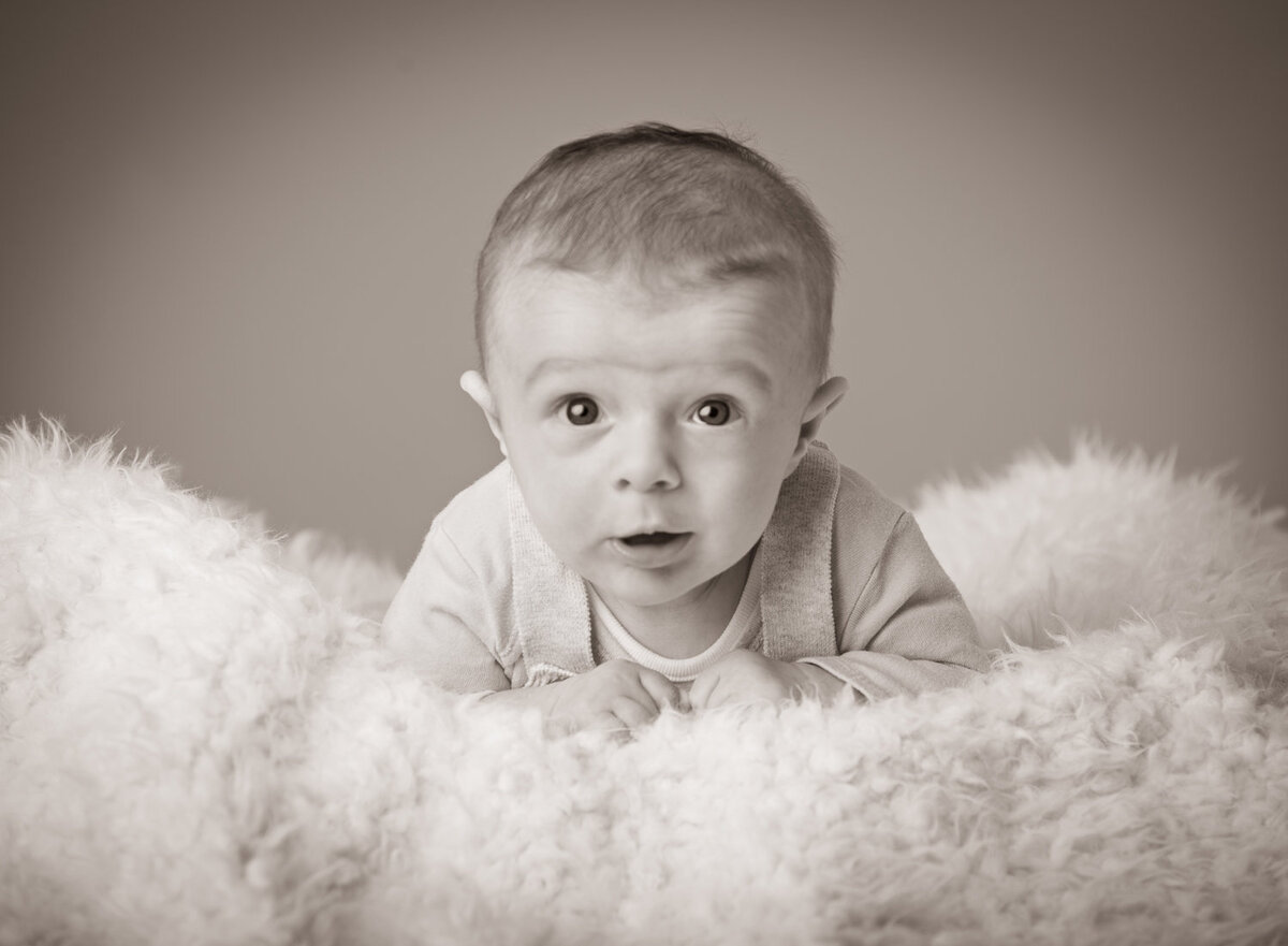 black & white portrait of a baby with dark hair lying on a fur blanket