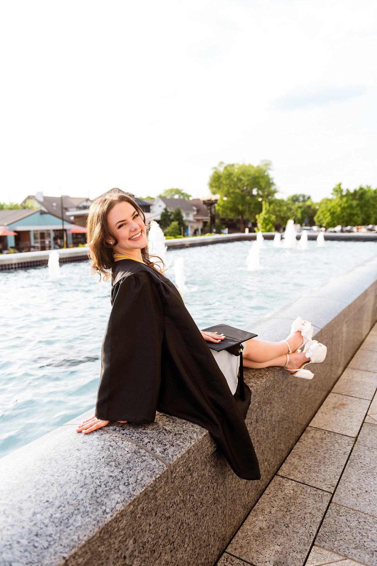 Senior wearing graduation gown sitting on fountain at Belmont University