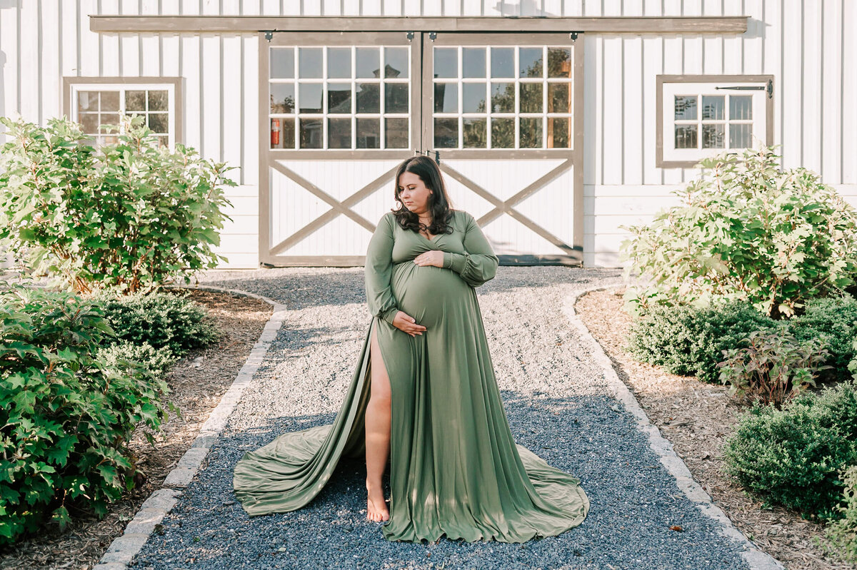 A woman holding her pregnant belly in front of white rustic barn doors