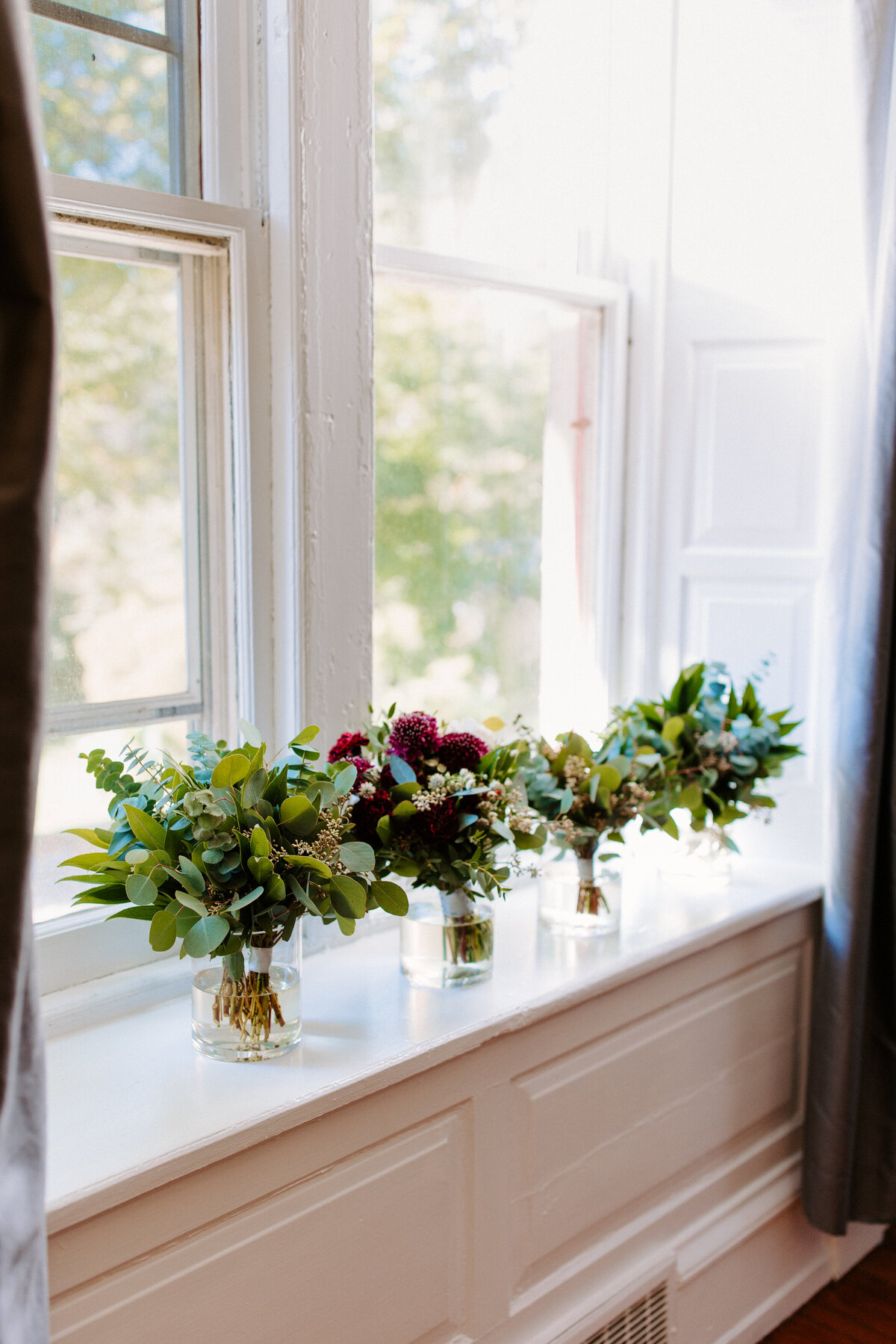 4 bouquets of flowers in vases lined along a windowsill