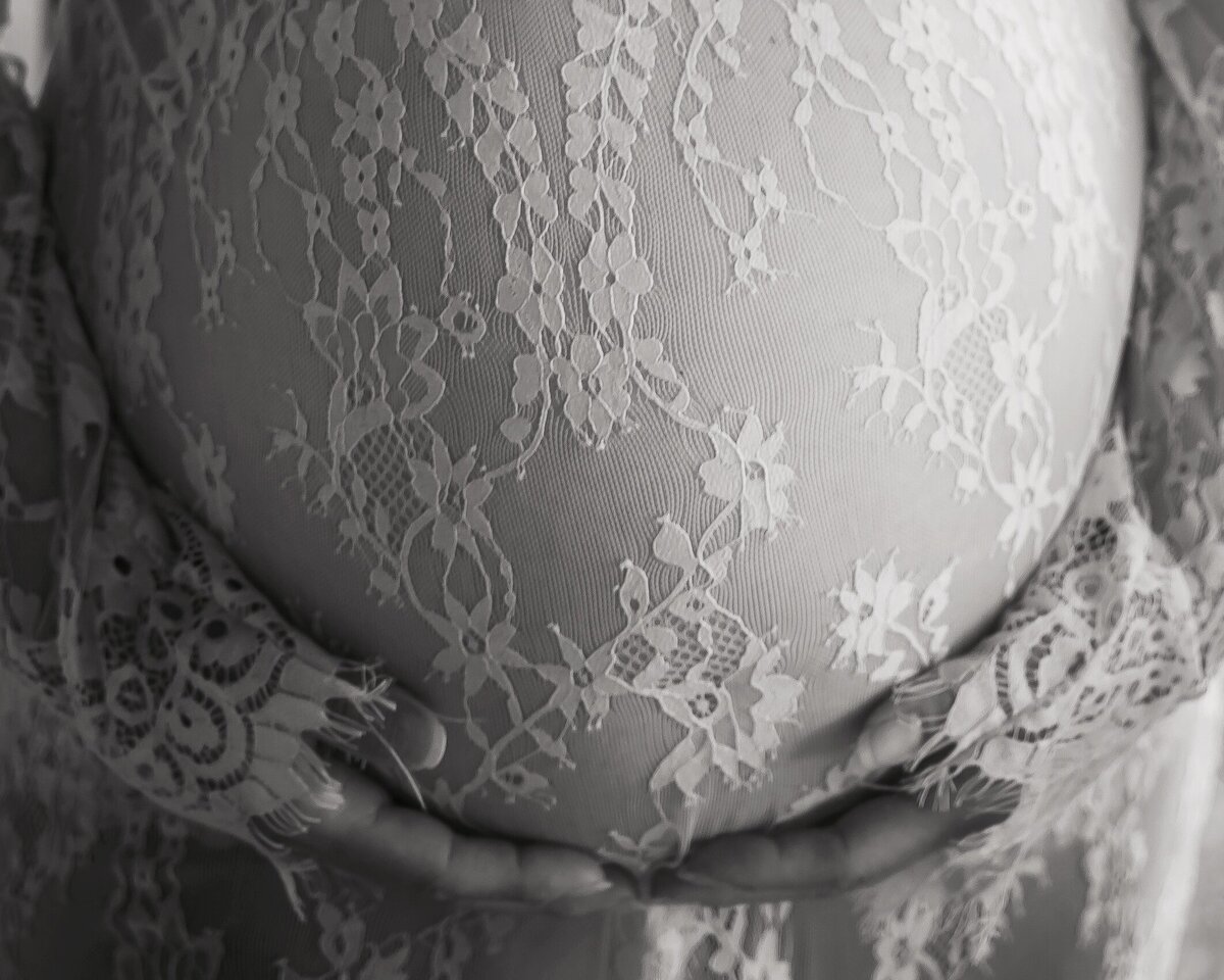 Hands hold pregnant belly covered in lace