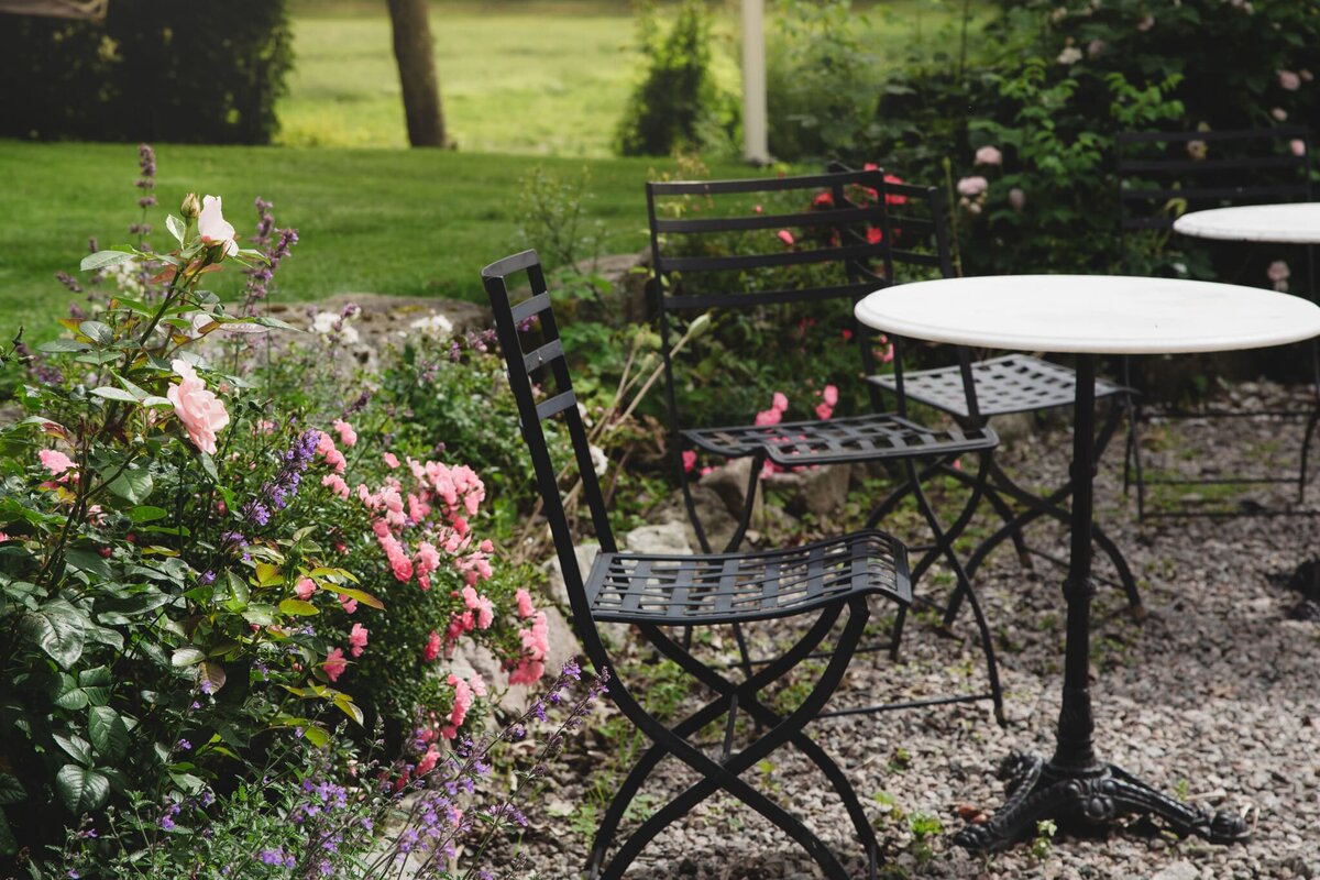 Verksamhetsbild från lantligt pensionat – blomstrande trädgård med cafébord i somrig miljö.