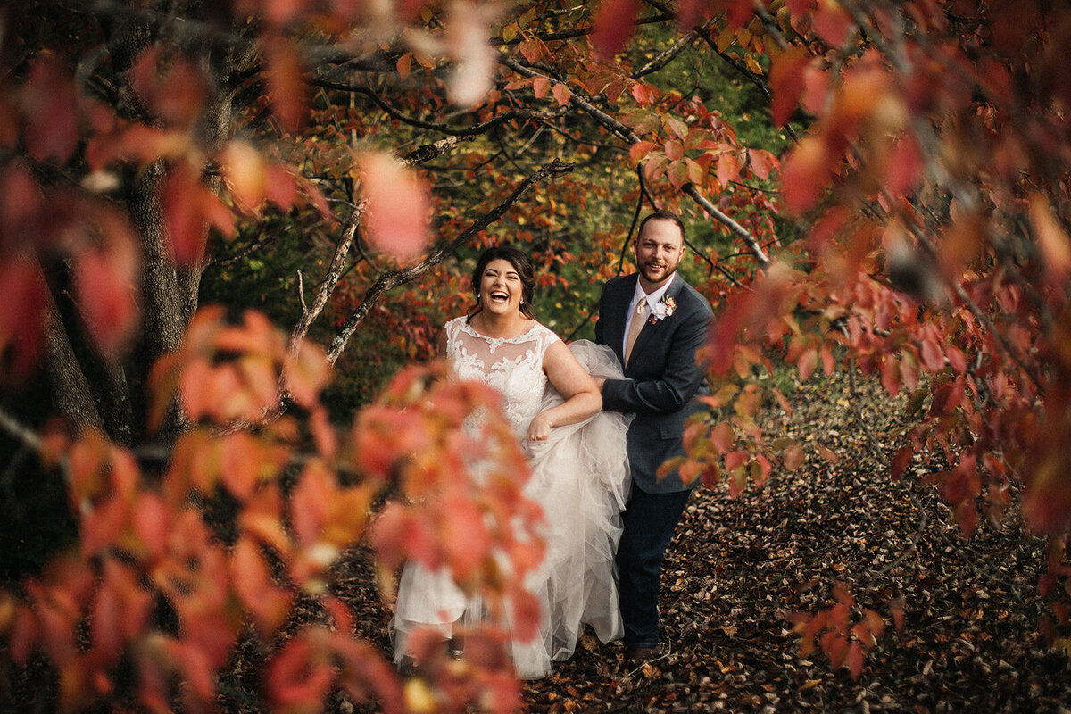 bride and groom walk through fall leaves