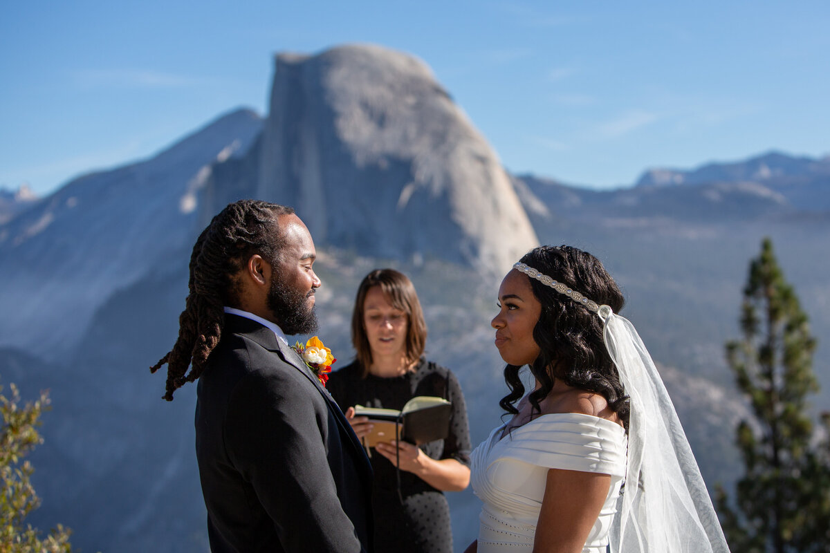 A bride and groom stand facing each other during their elopement ceremony with Half Dome in the background.