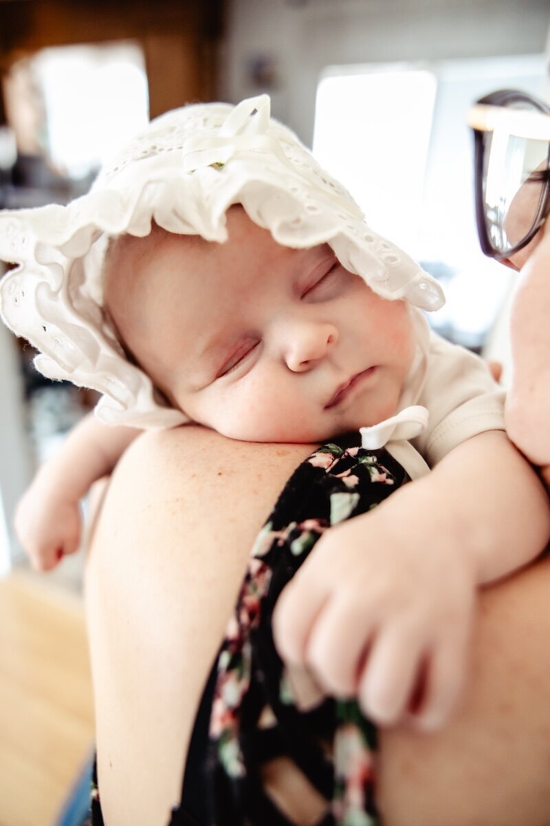 a baby girl wearing a bonnet sleeping on her mother's shoulder