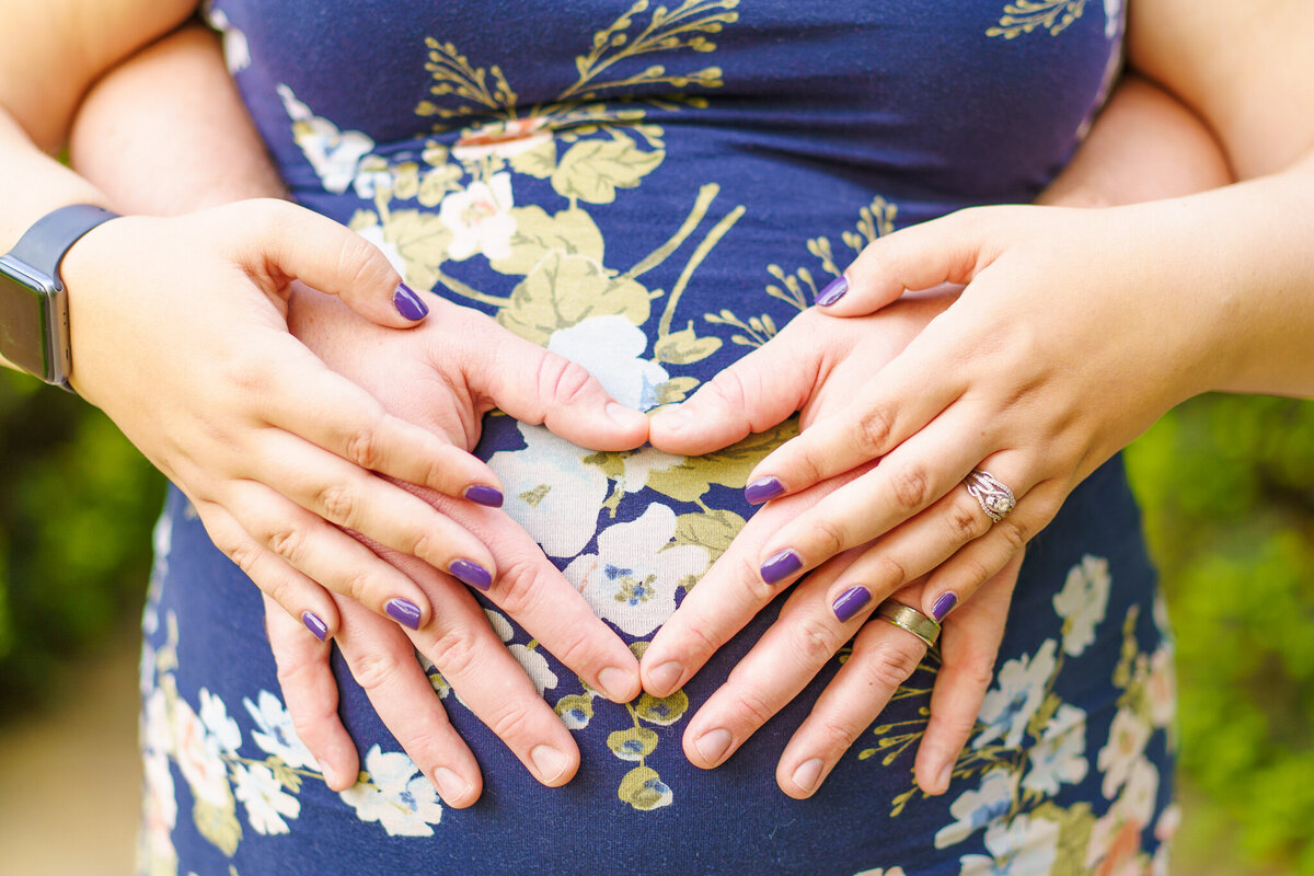 A husband places his hands to make a heart on his wife's belly and her hands are placed on his. - Maternity photo