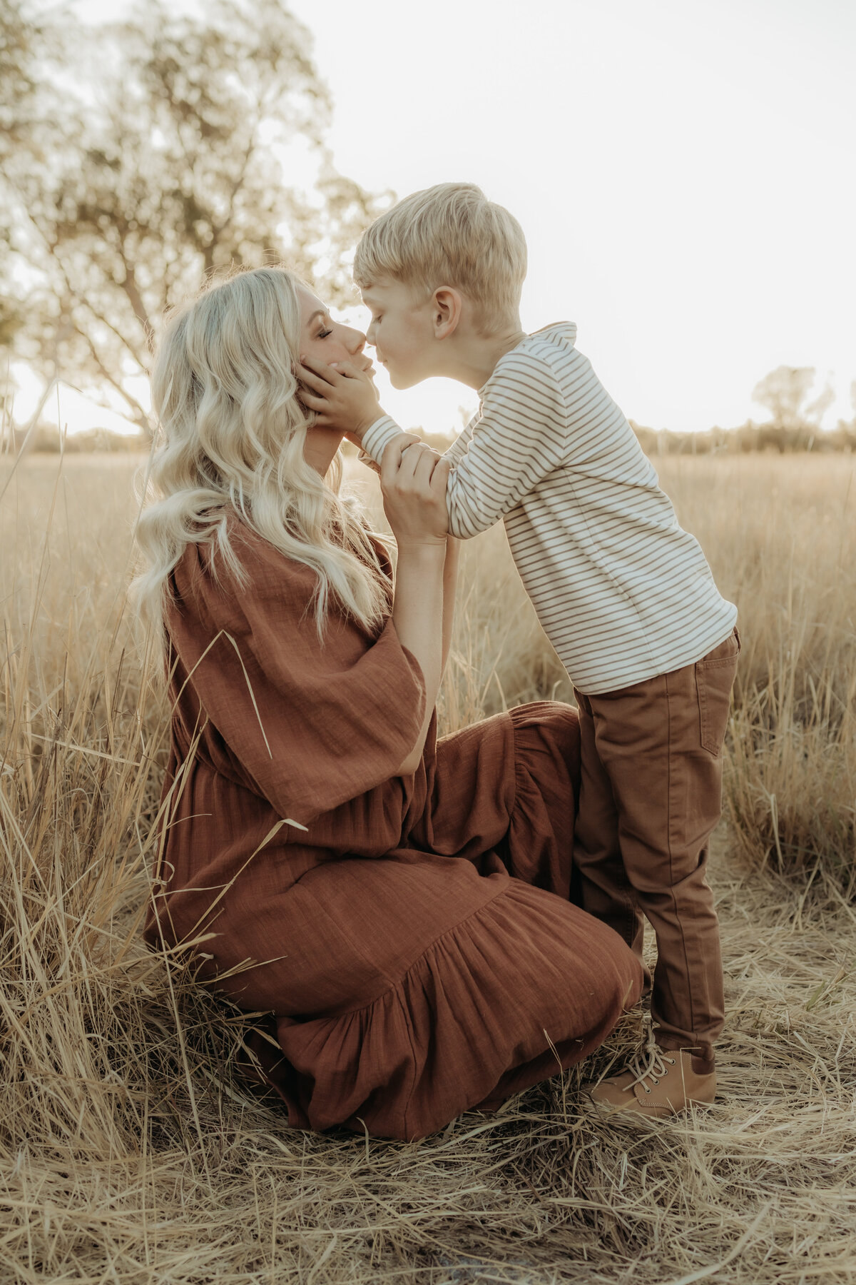 a boy holding his mums cheeks as they share a beautiful moment in front of the sunset, in a field in Perth WA