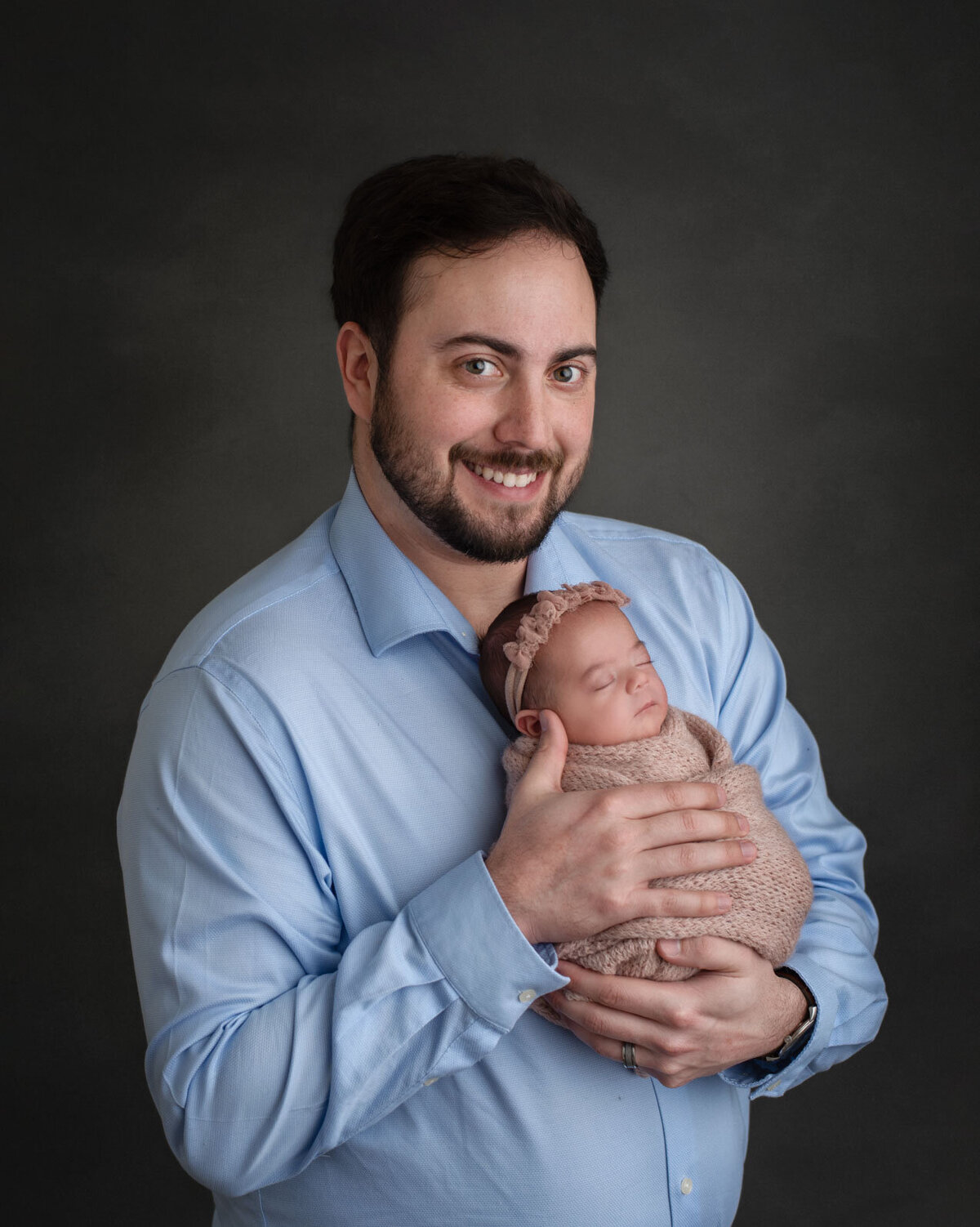Dad looking at camera and smiling while holding newborn in pink