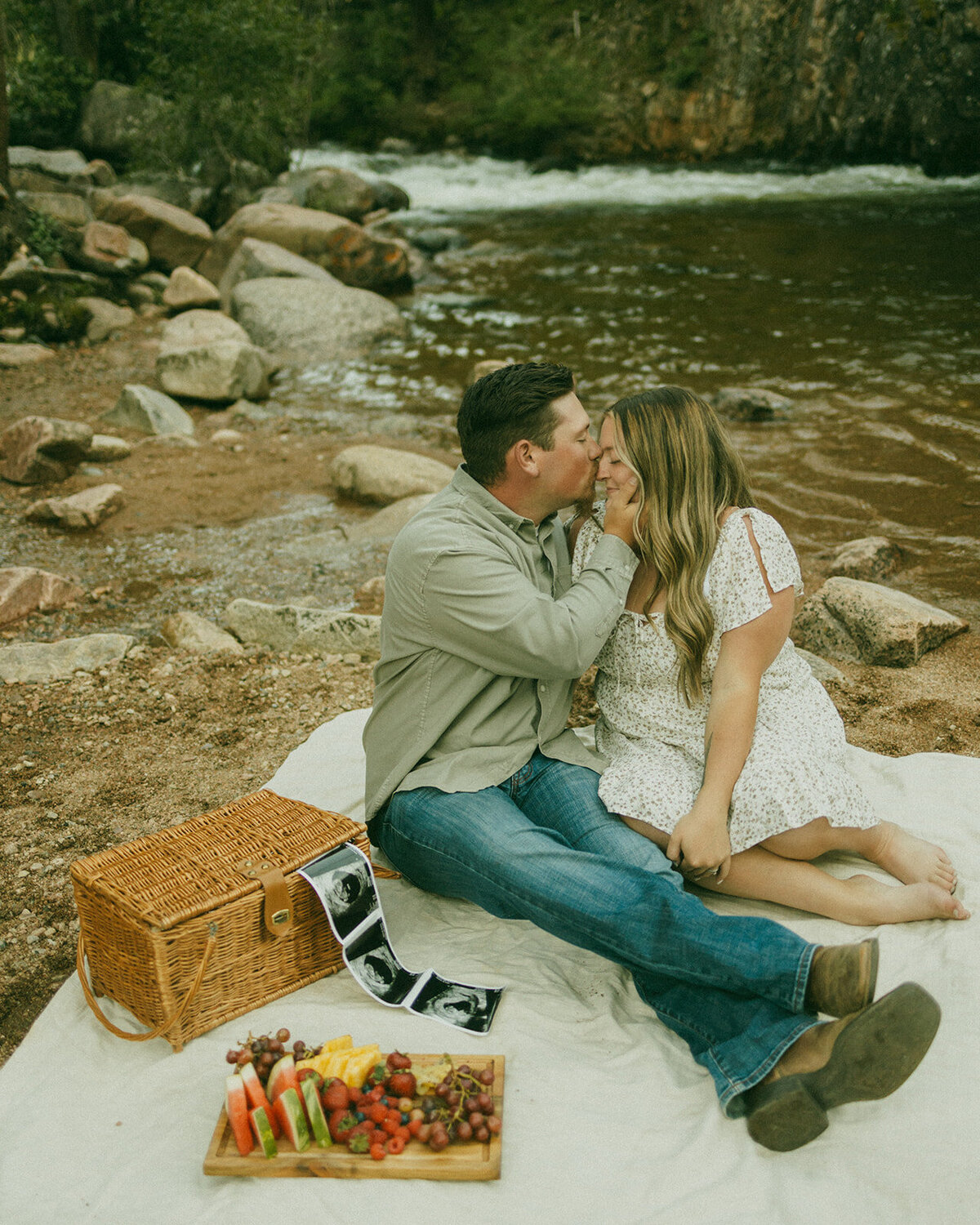 couple in front of water man kissing womans forhead with ultrasound pictures on blanket