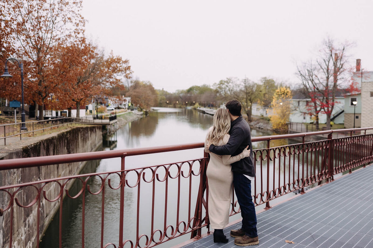Man and woman hugging looking out on river at at Finger Lakes maternity session