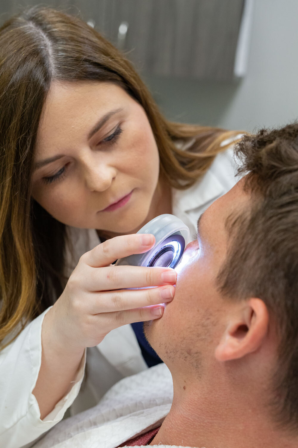 A woman is examining a man 's face with a light
