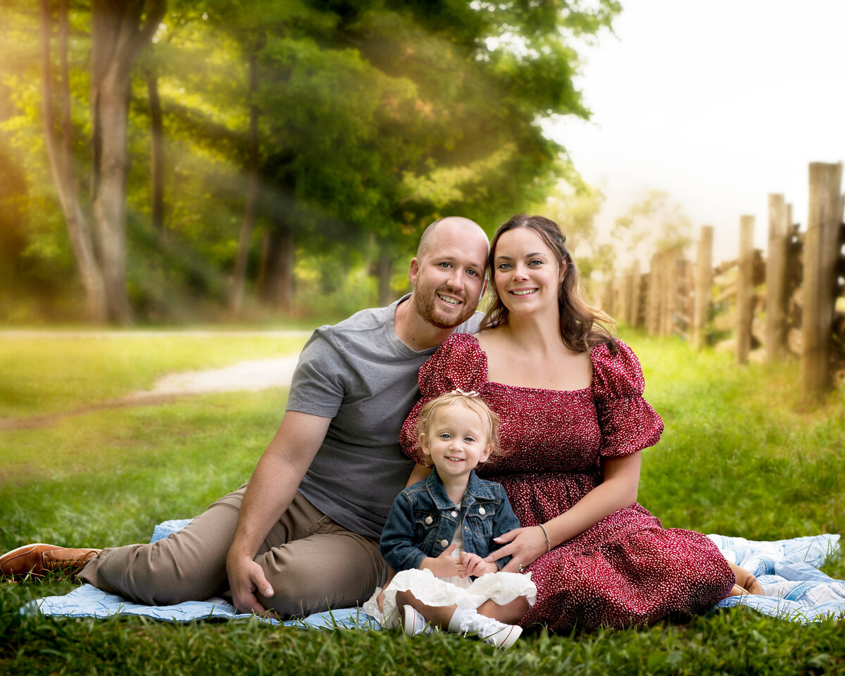 A joyful family sits on a quilt in Bronte Provincial Park in Oakville, Ontario, surrounded by golden summer light and rustic fences.