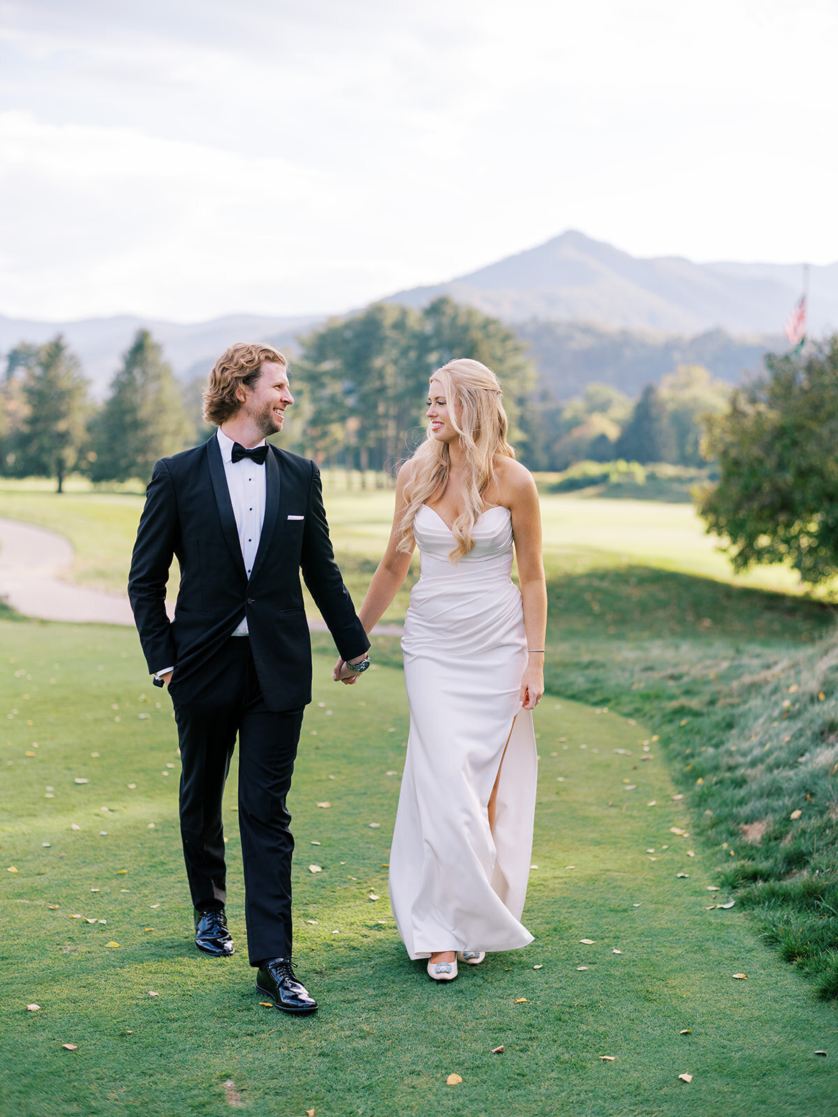 Bride and groom walking hand in hand on the golf course at Waynesville Inn with sweeping mountain views behind them.
