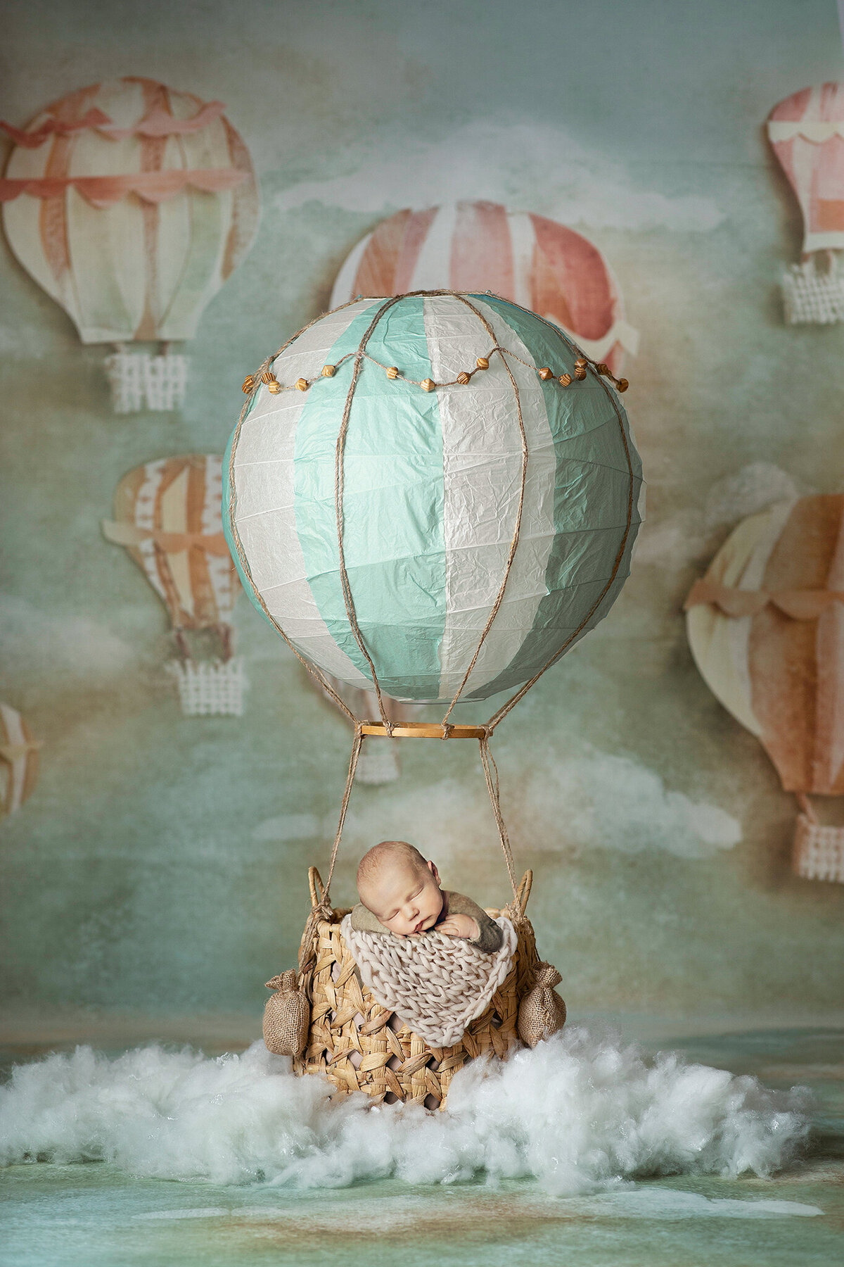 Sweet blond newborn boy posed in an air balloon prop with hot air balloon and cloud background