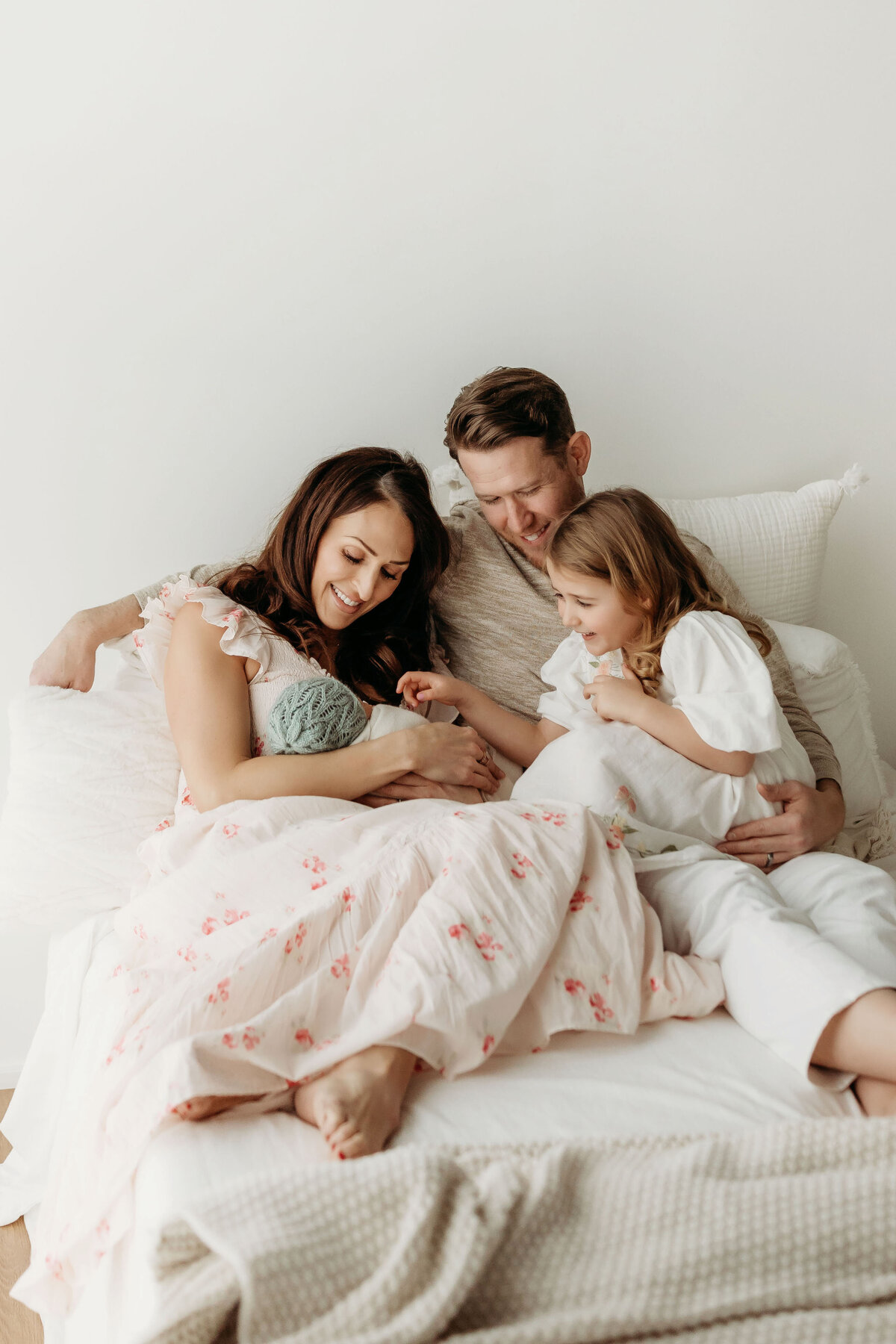 A family sits on a bed in beautiful natural light admiring their newborn baby, inside a Vancouver Washington studio