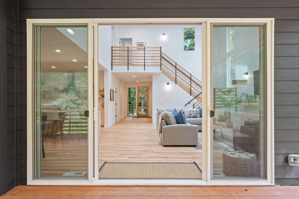 View through sliding glass doors into a bright, modern living room with wooden stairs