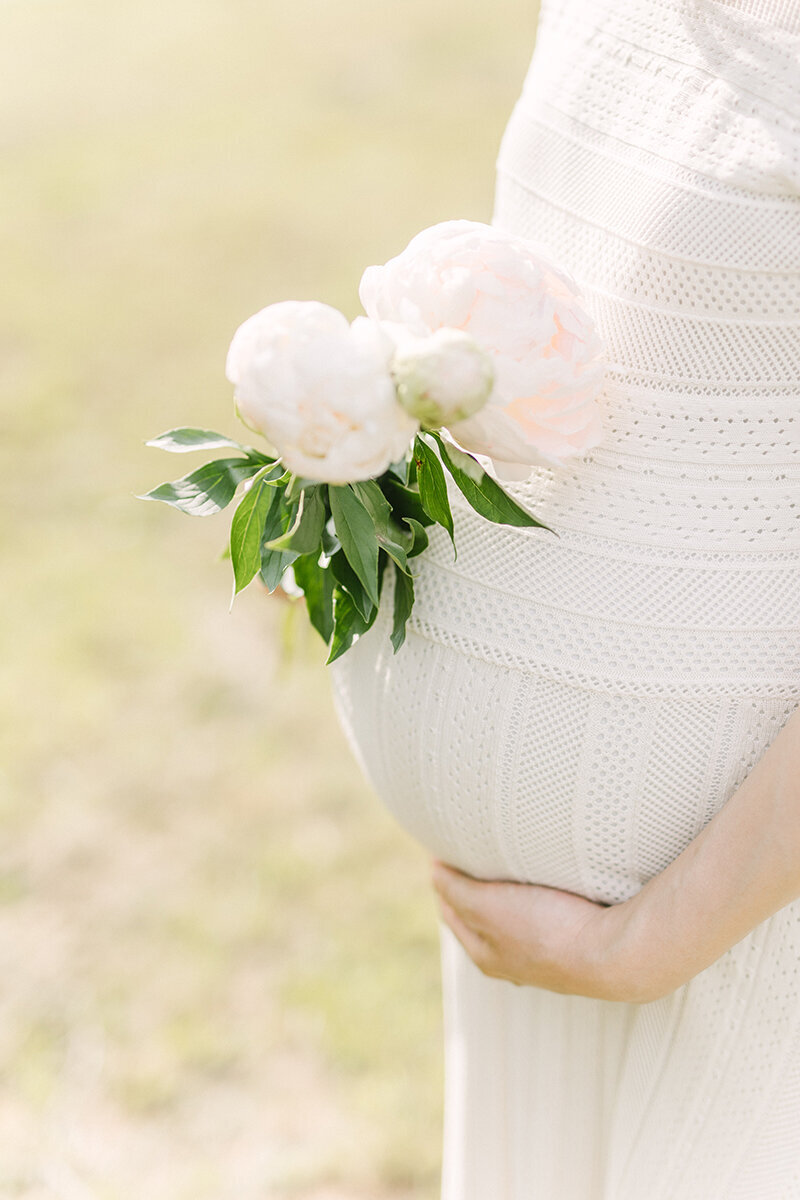 横浜市で撮影。ピンク色の芍薬の花と、丸くて大きい妊婦さんの妊娠9か月のおなかのおしゃれで美しいマタニティフォト