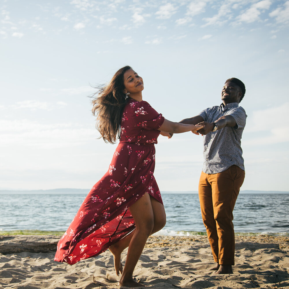 An engaged couple dancing with each other on a beach near Seattle.