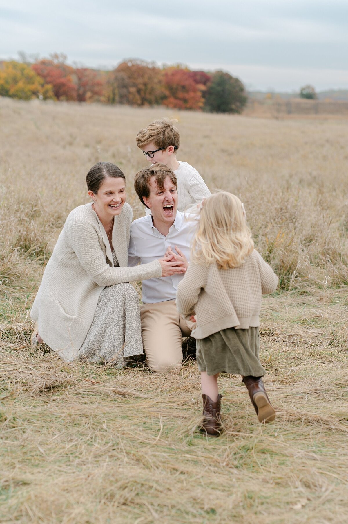 Little girl runs to her mom, dad and brother while they laugh and smile at her