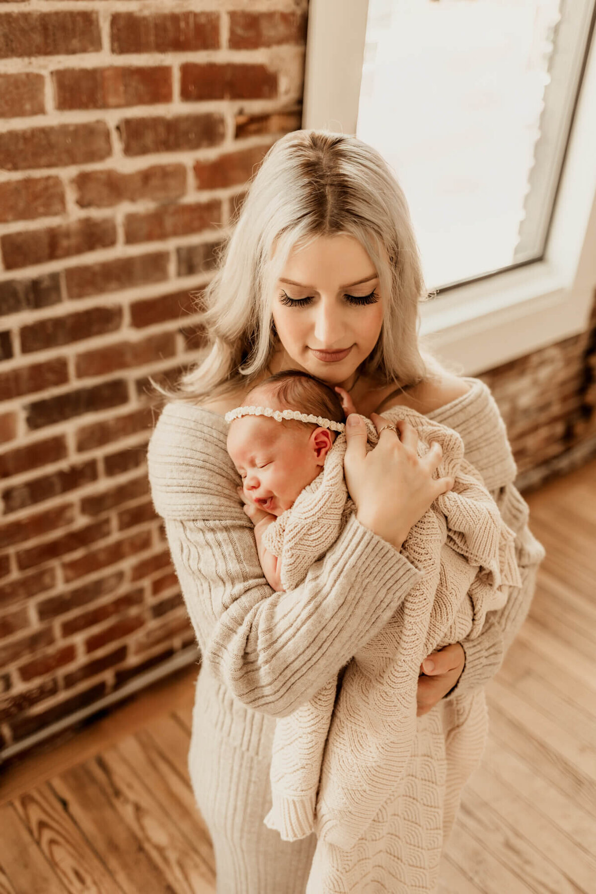 Mother holds her newborn daughter with a brick wall behind them for a newborn photo session in Jenks, Oklahoma.