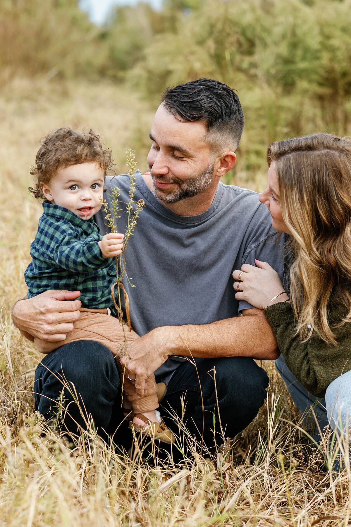 Happy family with young child sitting on grass in Wilmington park, outdoor family portrait