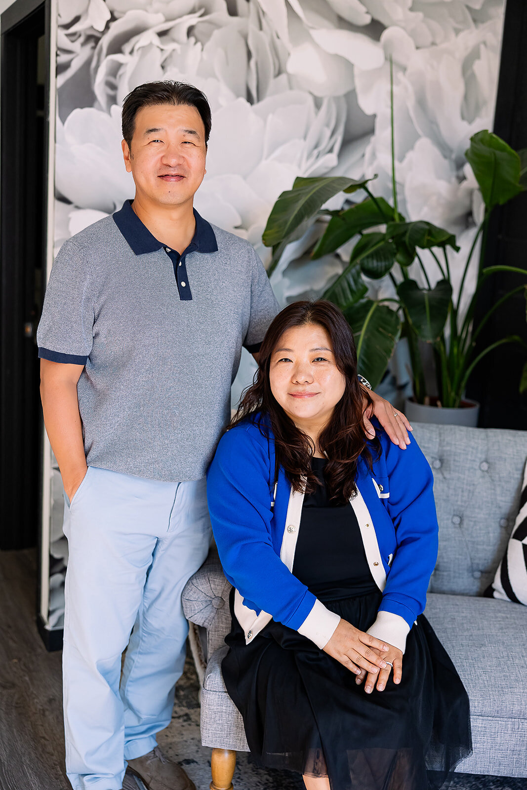 Man standing with his arm around woman's shoulder while sitting on a couch