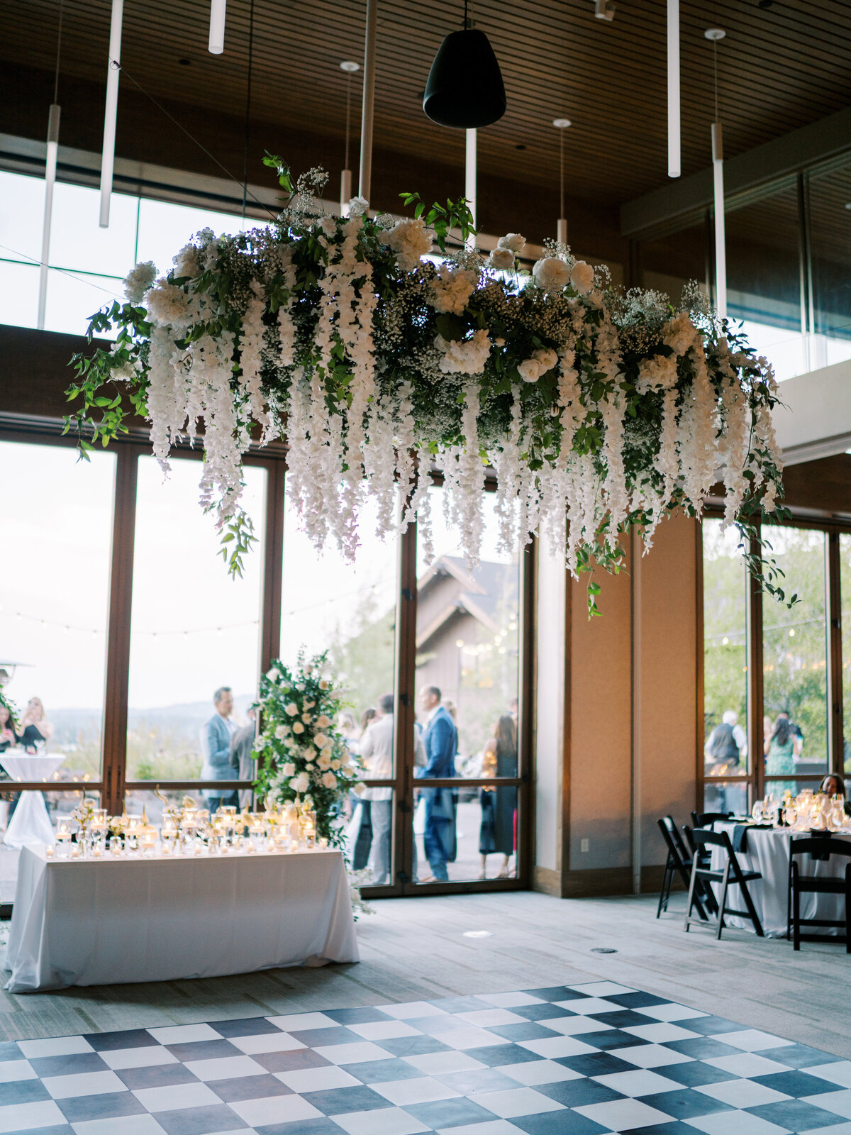 Hanging installation of white wisteria, hydrangea and roses with greenery over black and white checker dance floor in pavilion at Tetherow Resort in Bend Oregon