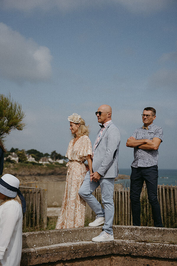Un couple d'invités observent la cérémonie face à l'océan. Scène capturée par Kamescop vidéaste et photographe mariage vintage.