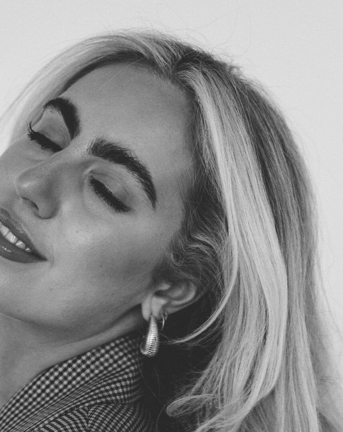 Black and white close-up of a woman’s face in profile wearing a hoop earring, with her long blonde hair swept to one side