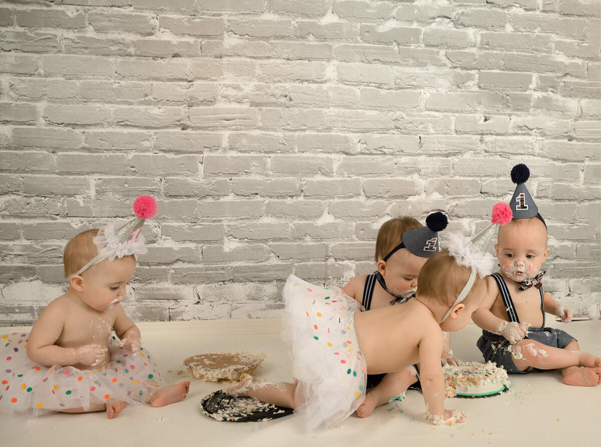 Quadruplets at their 1 year old cake smash. One of the girls is crawling over to steal some of her brothers cake.