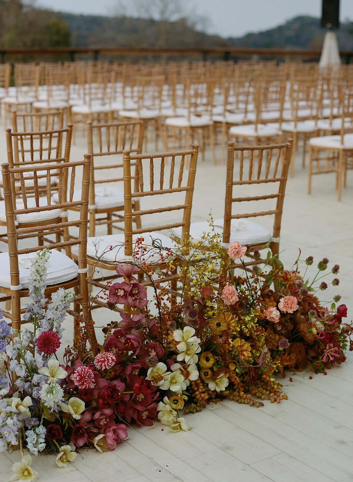 Product clustered floral meadows for entrance to wedding ceremony aisle. Unique fall wedding colors in copper, ruby, lavender, and gold. Artistic and sculptural floral design for fall wedding in Tennessee hills. Flowers featuring ranunculus, orchids, tulips, and dahlias. Custom build platform for private property wedding ceremony. Private home wedding ceremony and reception. Design by Rosemary & Finch Floral Design in Nashville, TN.