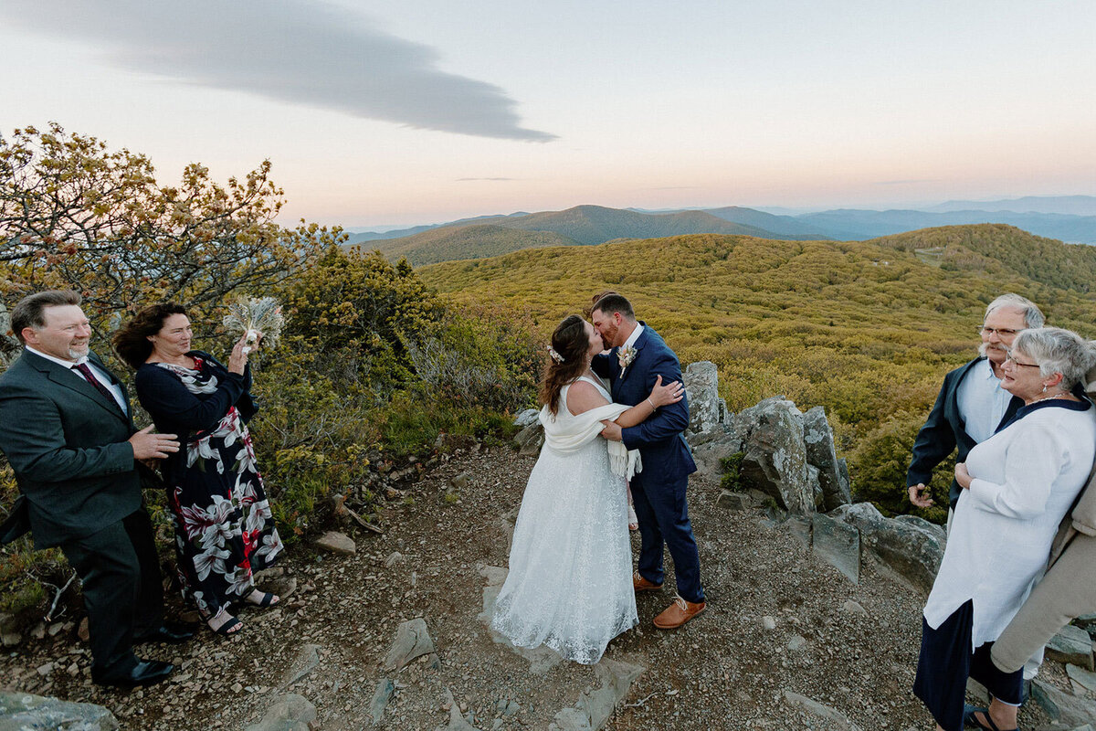 A bride and groom share their first kiss on their wedding day surrounded by their immediate family