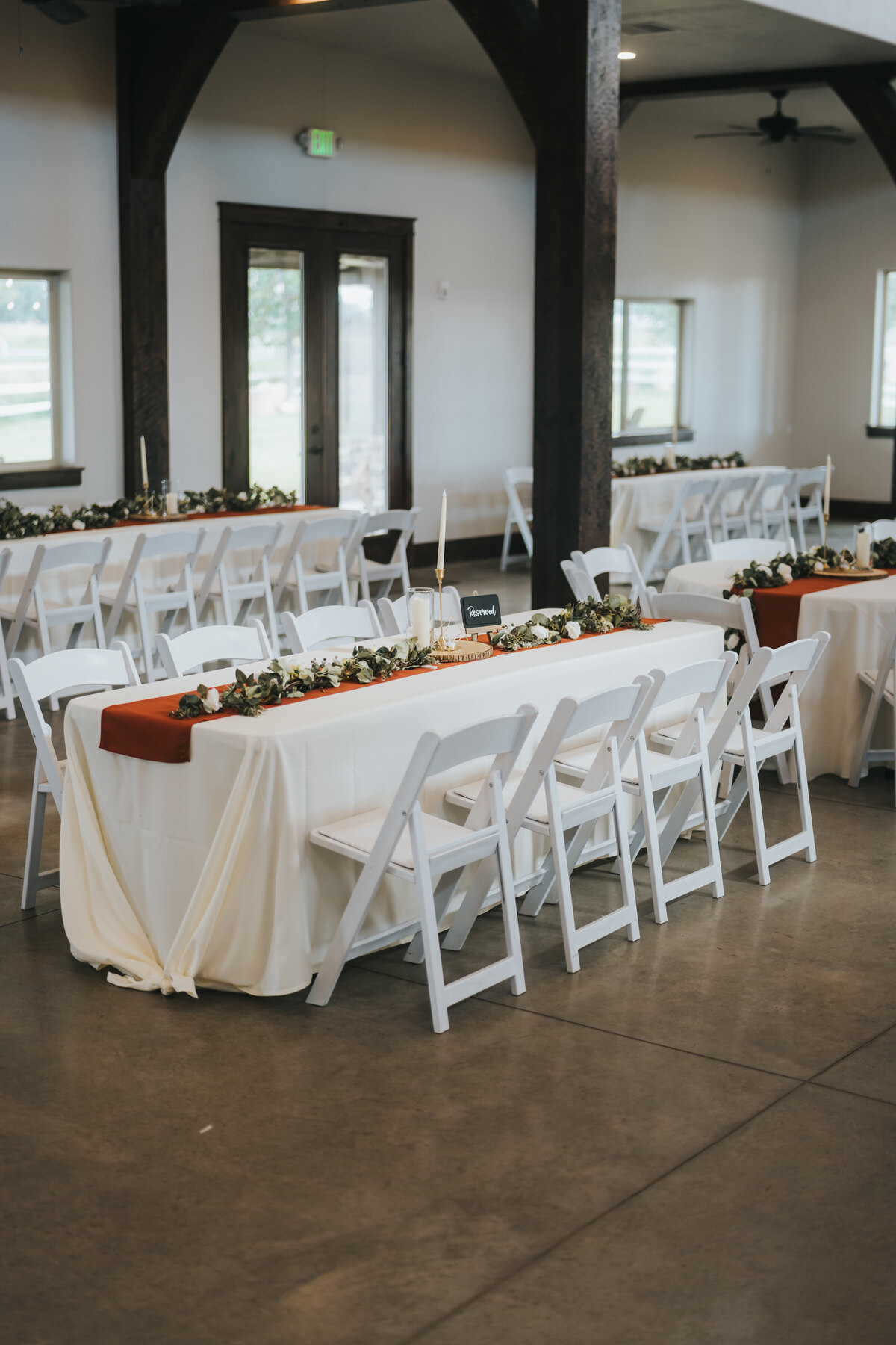Reception tables with greenery runners and white chairs in the grand hall