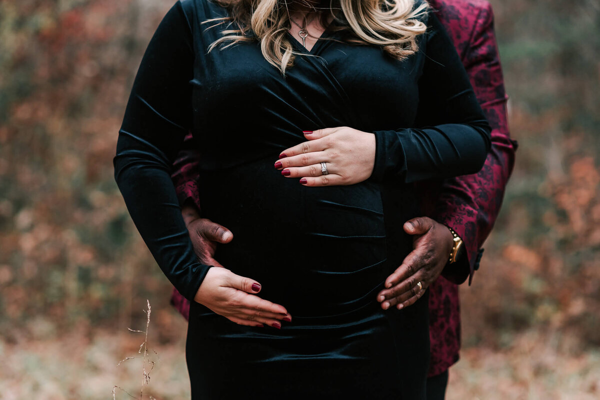 A front view of a woman's pregnant belly and her partner holding her from behind