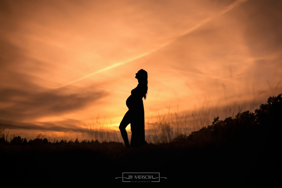 Een silhouette foto van een zwangere vrouw  met de zonsondergang op de achtergrond in de heide van Herperduin