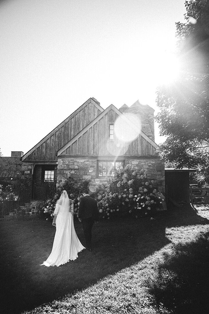 Bride and groom walking towards a house under a sunbeam of light in black and white photo. Captured by Mira Park Photography.