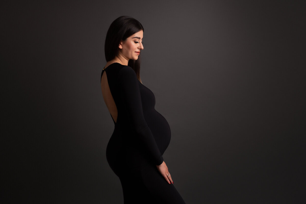 London studio side portrait of a pregnant woman wearing a classic long black dress with an open back.