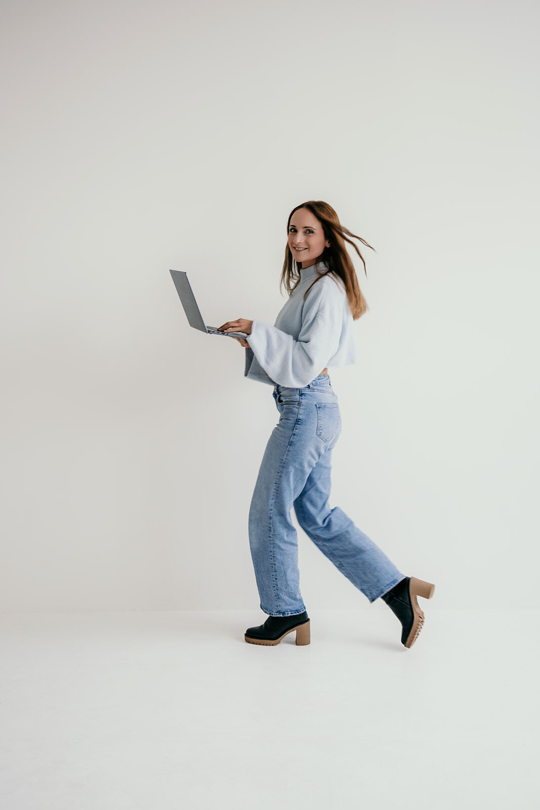 Woman walking through the room with a laptop in her hands.