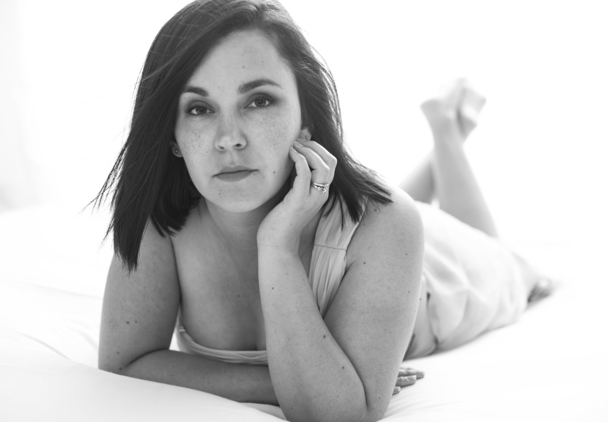 A woman with dark hair lying down posing on a high key white backdrop at Janel Lee Photography studios in Cincinnati Ohio