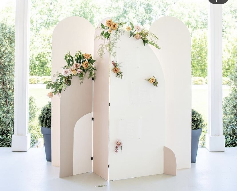 Neutral colored backdrop design made of arches and decorated with florals and greenery