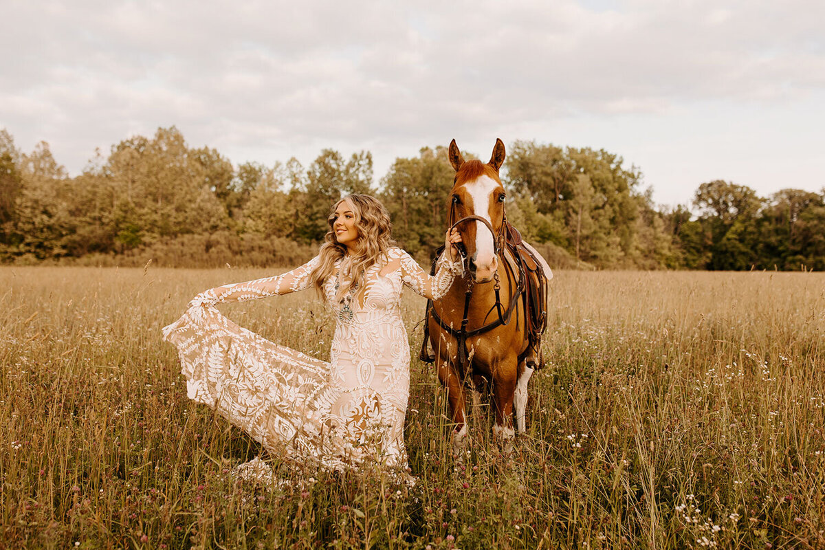 Bride in a lace gown holding her horse’s reins in a field