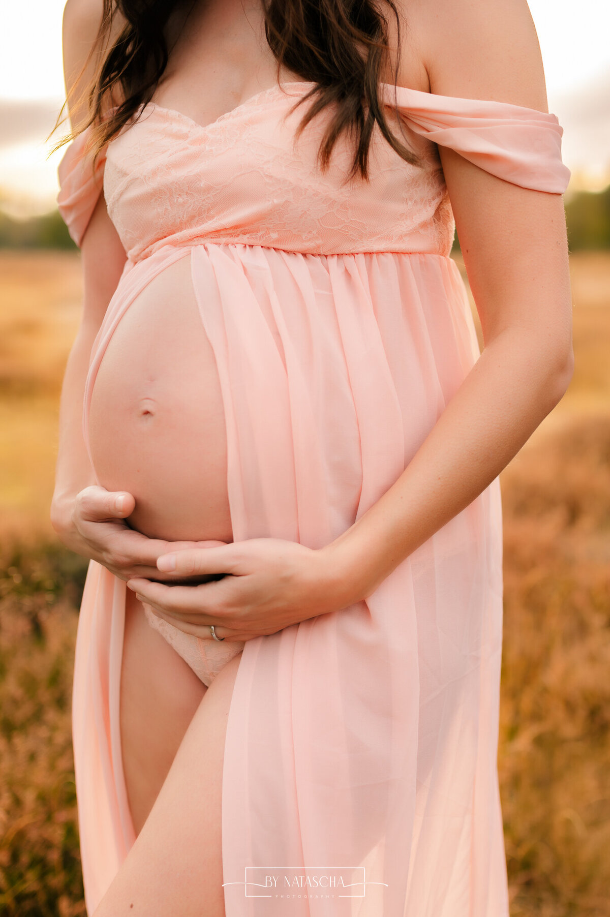Zwangere vrouw houdt met beide armen aan de onderzijde haar buik vast in de heide van Herperduin