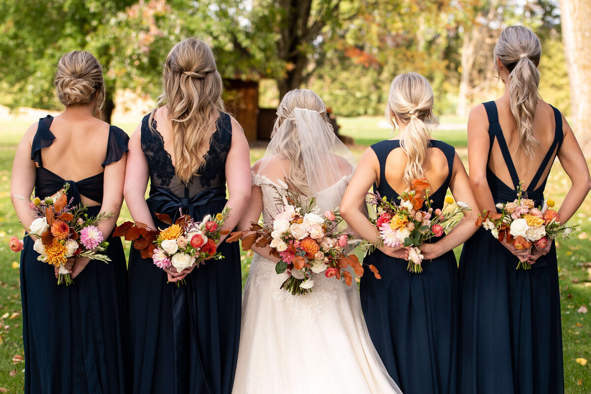 Ottawa wedding photography showing the different back details of five bridesmaid dresses.  The bridesmaids are holding their fall bouquets behind their backs