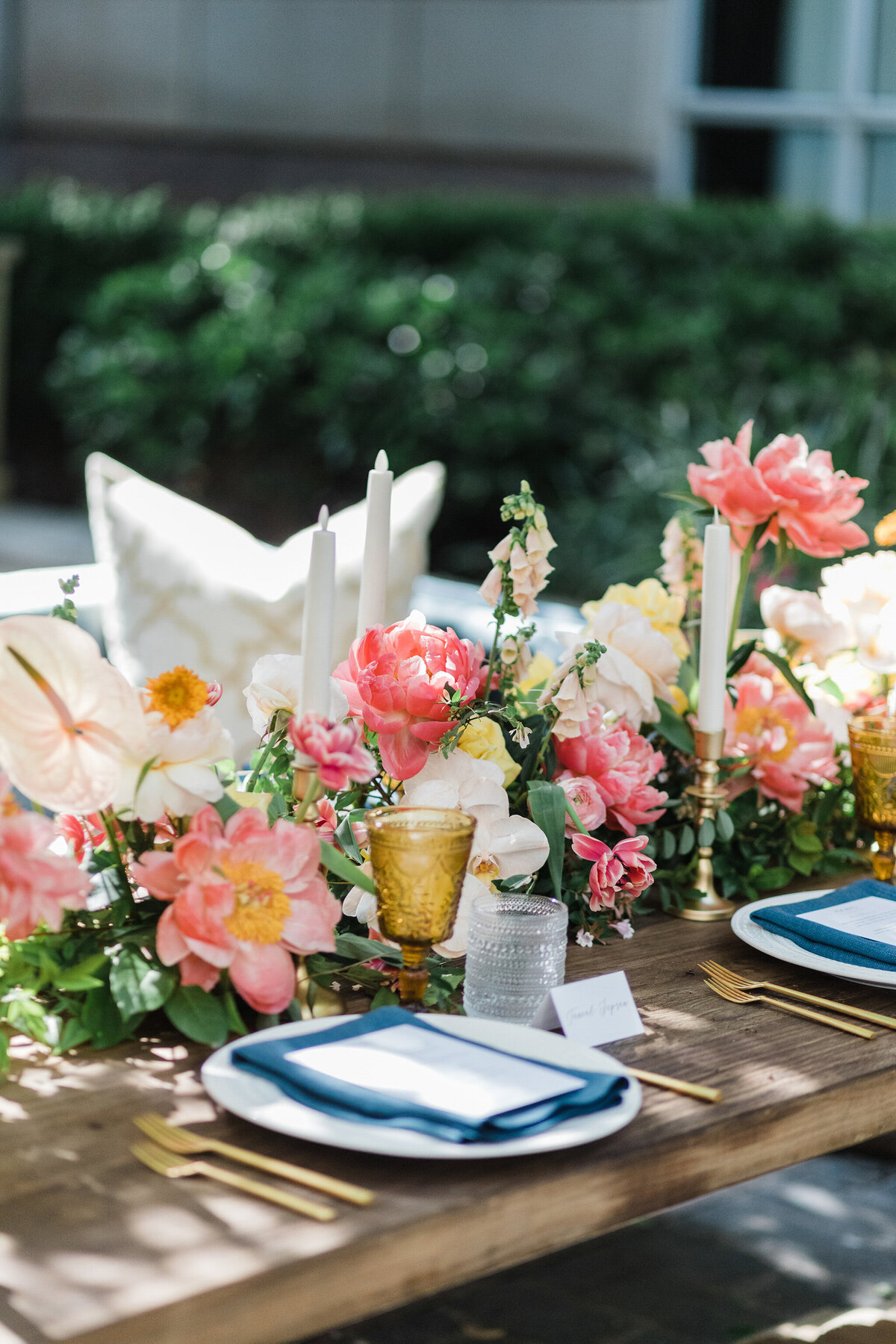 Detail shot of a place setting and reception table at the Hotel Crescent Court in Dallas, Texas. The place setting is made up of a white plate, blue and white napkin, and gold cutlery with two glasses. Surrounding it are candles and a large, long floral centerpiece.