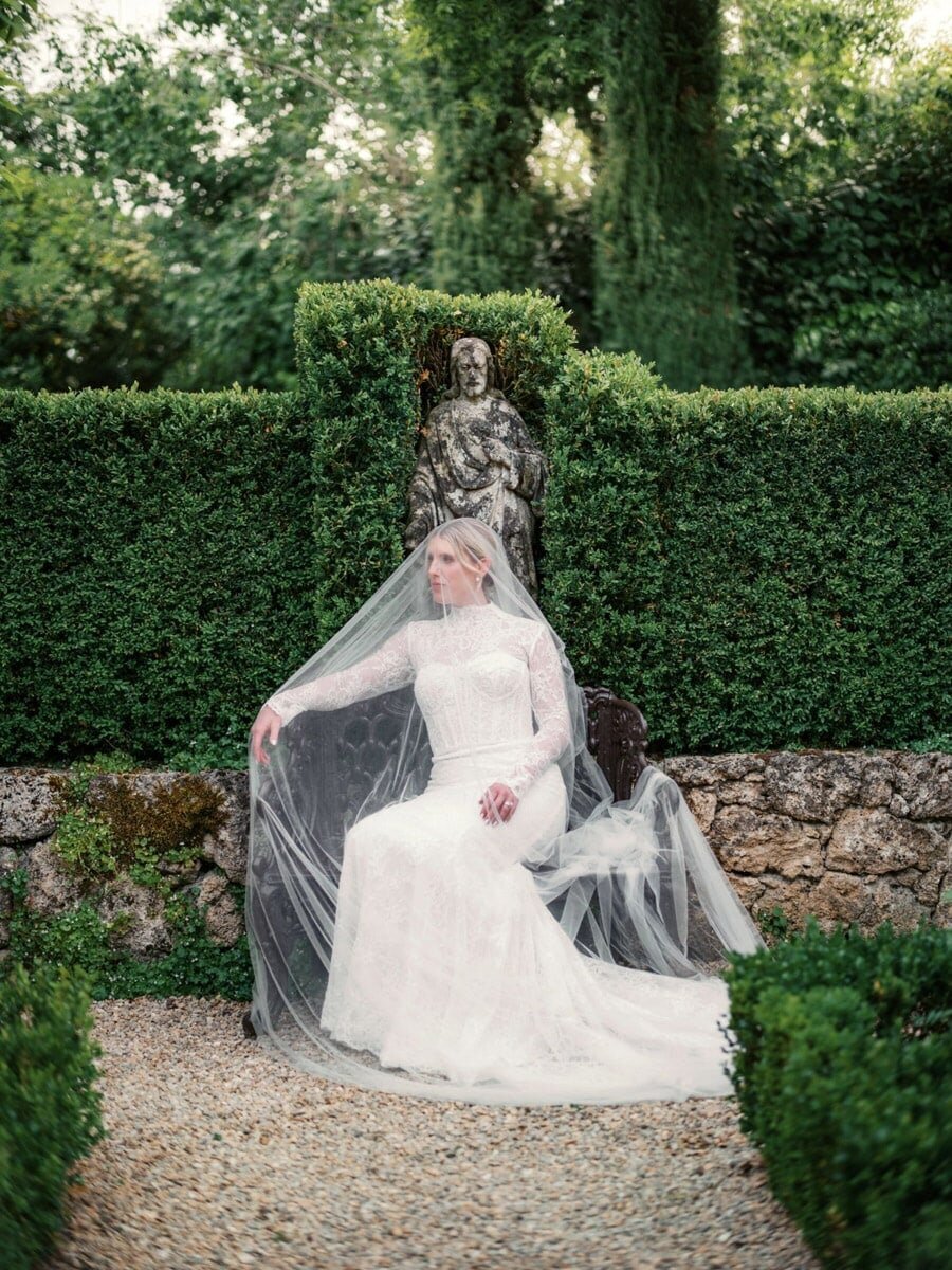 Outdoor bridal portrait of bride under veil, sitting on stone bench during a Borgo Santo Pietro Wedding 