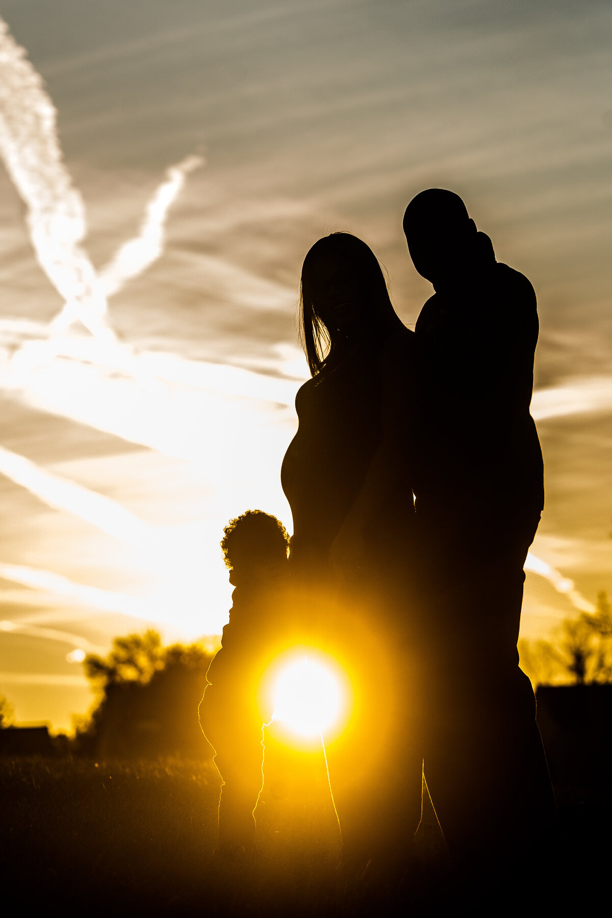 a family pose in front of a sunset for their maternity photos in Austin