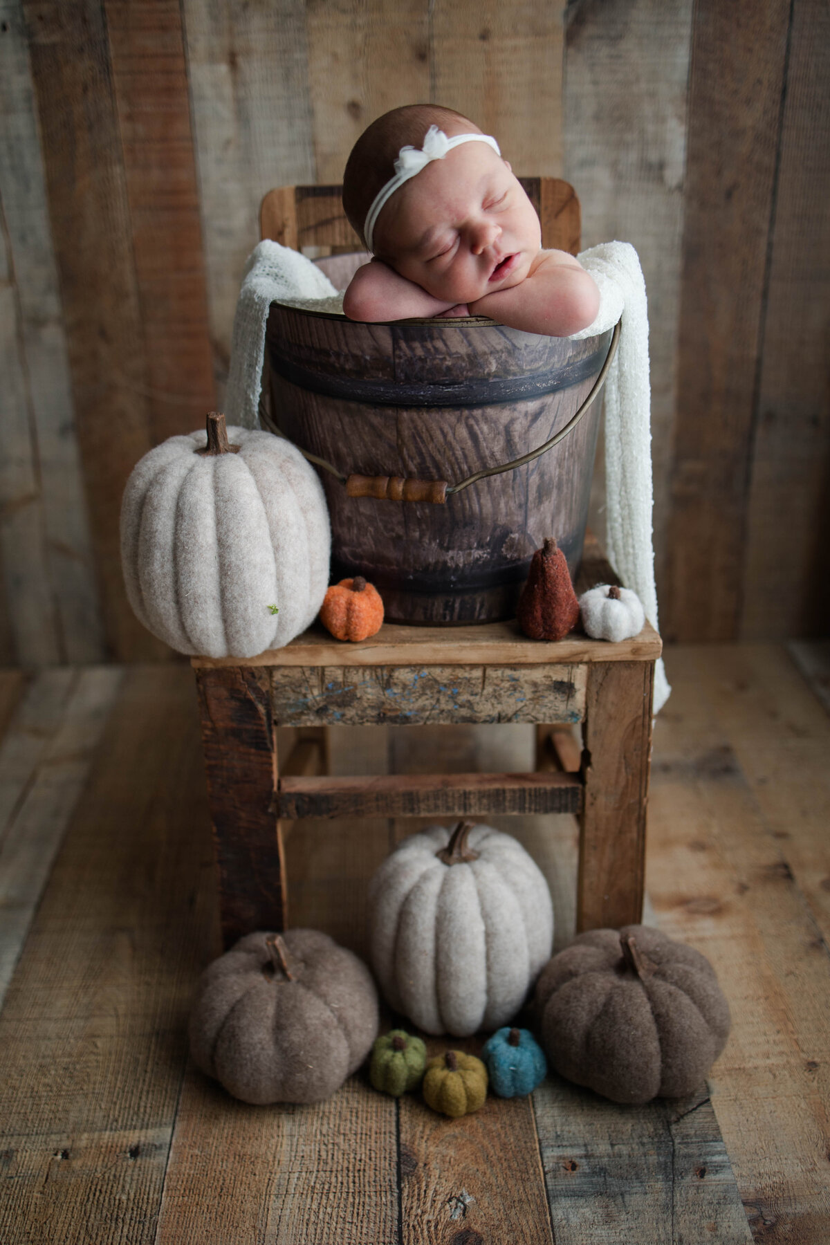 Newborn baby girl sleeping in a basket surrounded by pumpkins