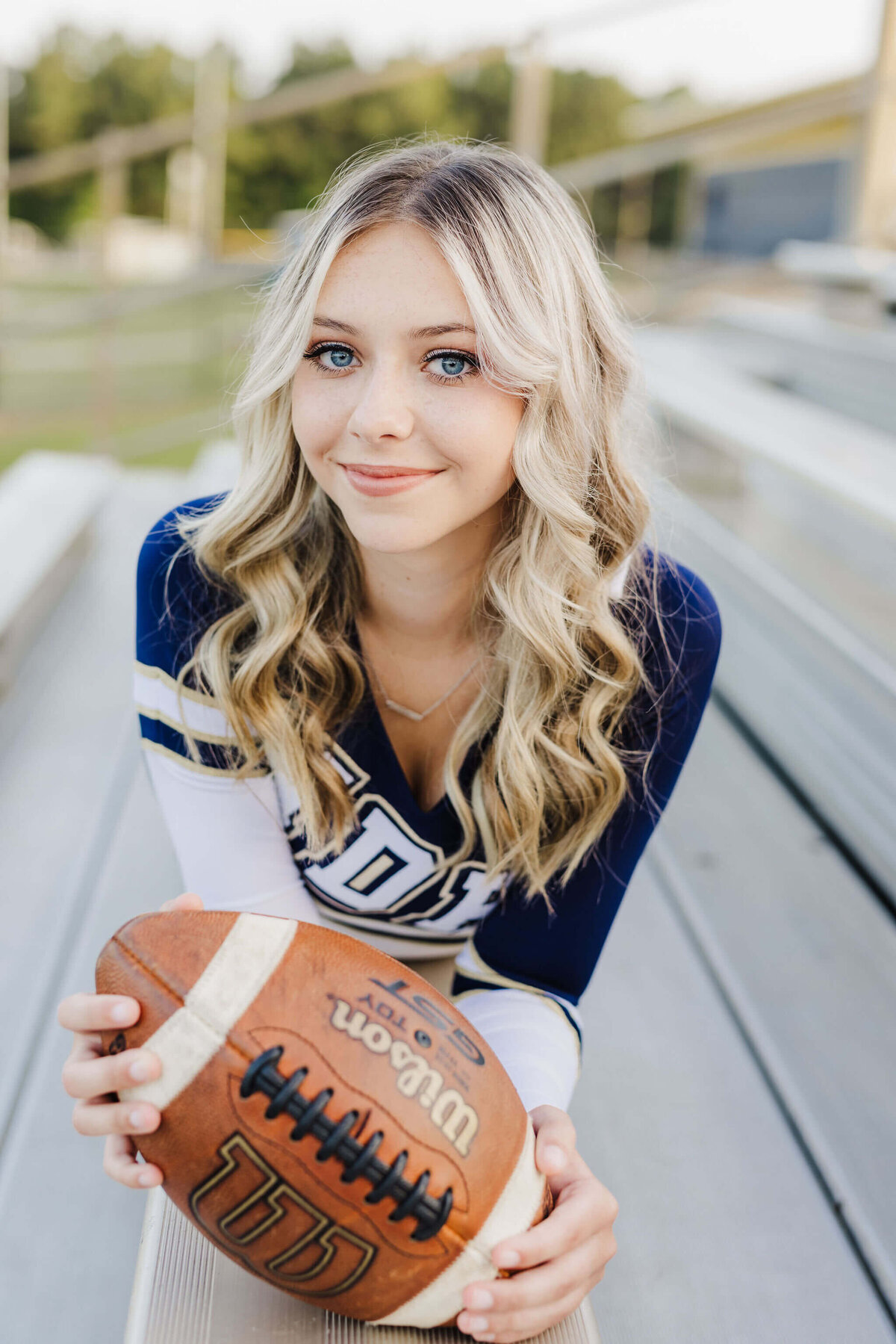 New Diana senior cheerleader wearing cheer uniform lying in football stadium bleachers while holding game day football