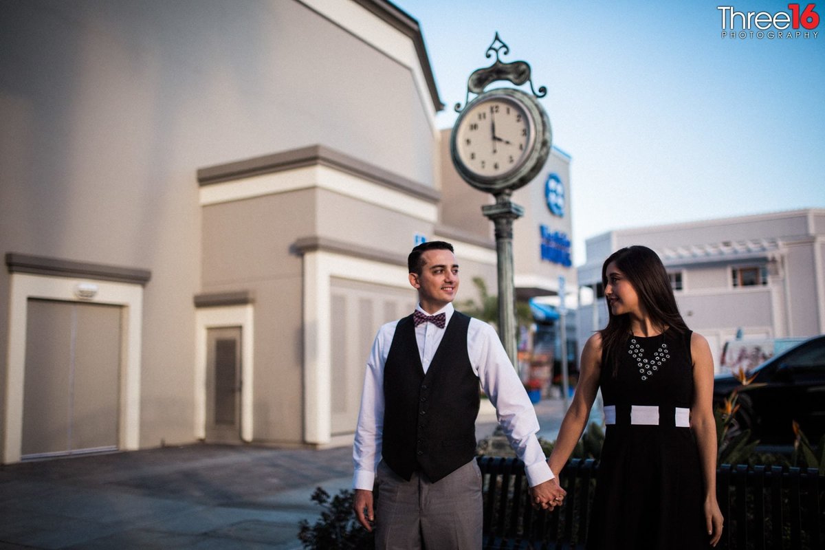 Engaged couple look at each other while holding hands in front of the town clock