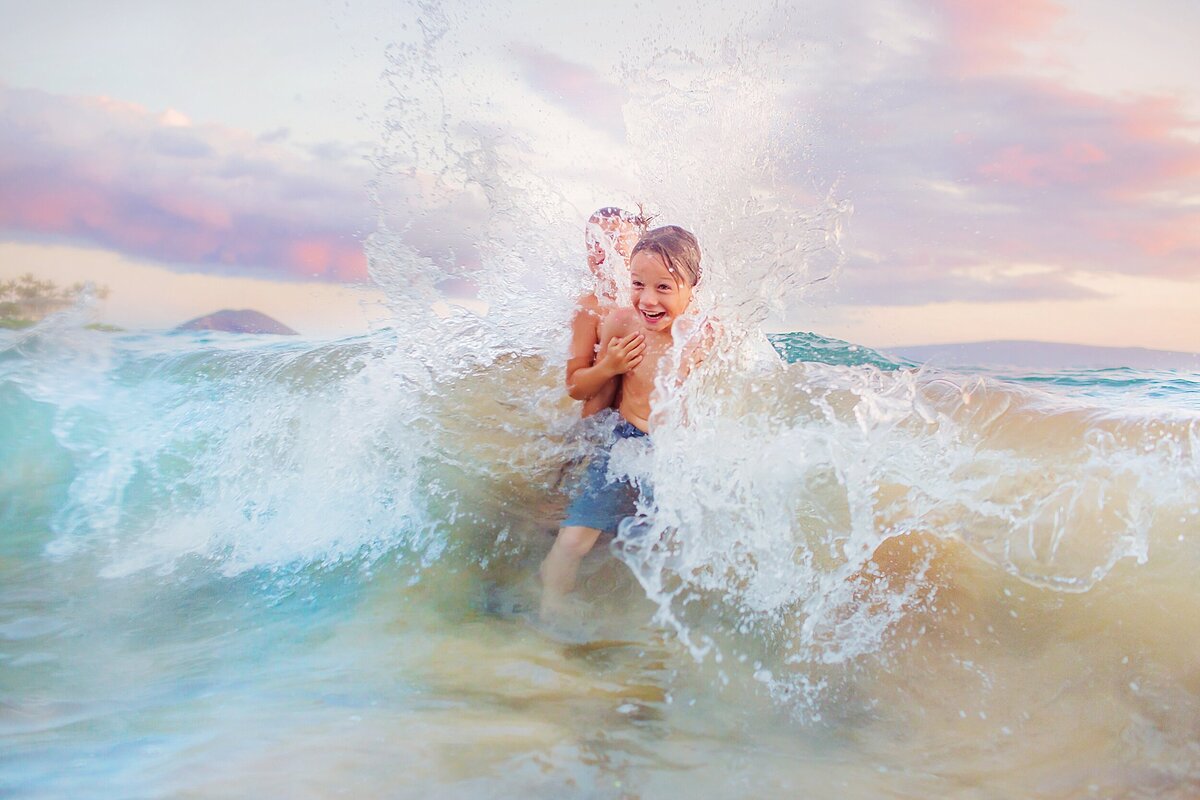 Two boys laughing as a wave crashes on the shoreline for a candid portrait in the ocean on Maui